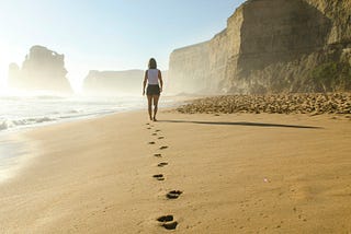 A woman walking along a beach, leaving footprints in the sand