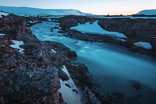 A steaming geothermal river in Iceland flowing through black volcanic rock