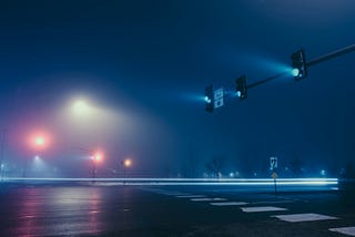 An empty street with a green street light. The concrete is wet.
