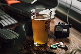 A glass of beer next to a keyboard and office equipment.