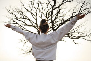 Person exercising with arms raised in front of a tree