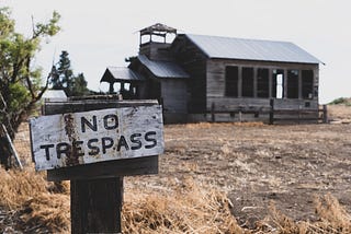 A “No trespass” sign sits in front of an old, wooden house in the countryside