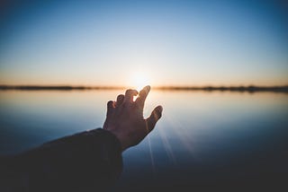 A hand reaching out to the sunlight over the sea and the horizon