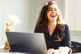 Woman smiling at desk with laptop next to trophy.