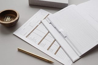 Gold colored stationery layed out with paperclips, a pen, notebook paper and a planner.