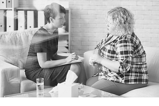 Two people sit in a corner, having serious conversation. One of them holds a clipboard