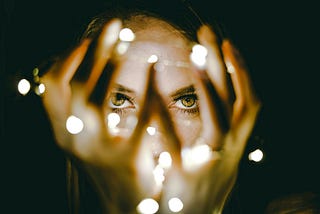 A person holds their hands in front of their face. Small points of light float around their hands.