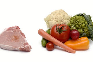 Left: a raw steak. Right: A pile of vegetables, including a carrot, tomatoes, broccoli, cauliflower, and a bell pepper