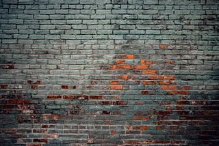 An old brick wall with mostly grey bricks some bricks are coloured orange and some are dark red.