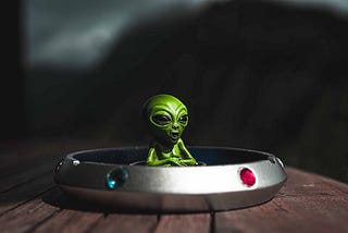 A green alien sitting in small spaceship