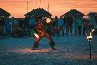 A man playing with fire at sunset on a beach.