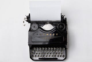 Black vintage Adler ‘Favorit’ typewriter with a blank page against a blank white background.