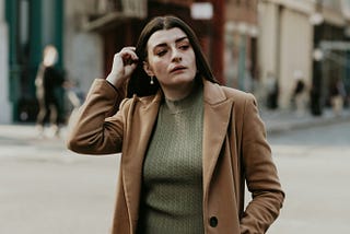 woman in brown coat standing on sidewalk during daytime