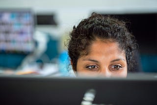 Person with curly hair intently looking at a computer screen, symbolizing the focus and vigilance needed in cybersecurity to avoid social engineering threats.