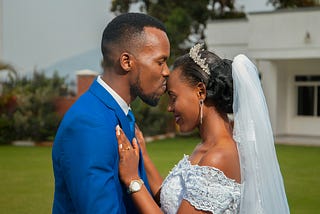 Man in blue suit kissing woman in bridal gown on forehead