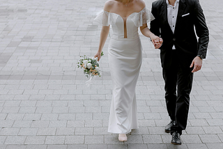 A bride and a groom holding hands outside.