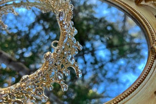A sparkling royal crown sits atop a mirror that reflects trees and sky