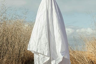 Single ghost standing in dunes of beach.