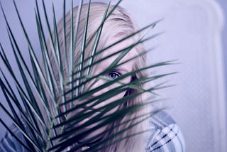 Blonde woman peeking out from behind a houseplant