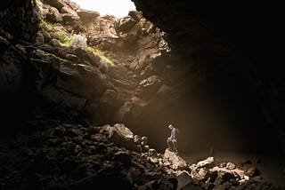 A lone hiker walking up steep rocks to reach the light at the top