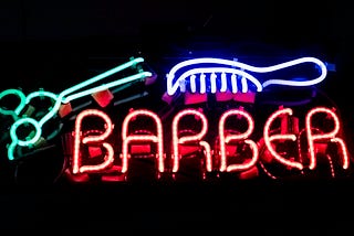 Neon sign with the word ‘barber’ in orange, a pink comb and green scissors.