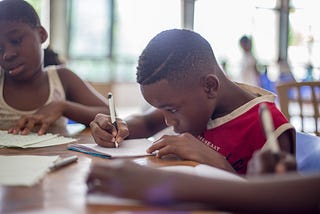 A boy writing in a book. His focus is as if he were writing some lines of codes.