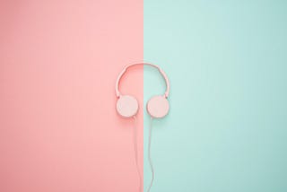 A pair pink of headphones with a pink wire is placed in the centre of the image. The background is split down the middle. The left side is pink, the right side is green.