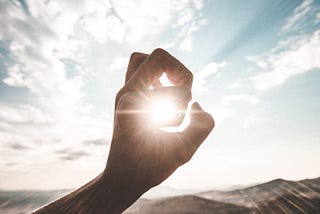 fingers making an ok symbol super impossed over the sky ans sun