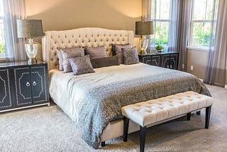 Beautifully designed bedroom in shades of tan, including perfectly-made bed, dresser drawers and curtained windows