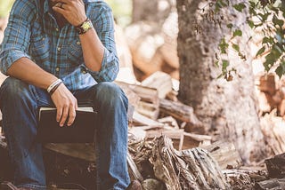 Man sitting next to cut wood while holding a journal