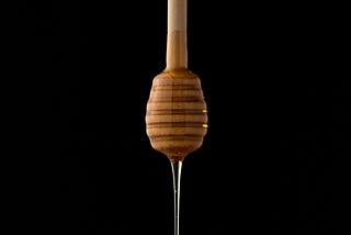 A honey stick dripping honey on a black background.