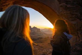Two women looking out at the sunset under an old arch, the world full of possibilities