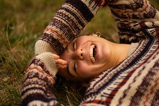 A woman laying in the grass, laughing.