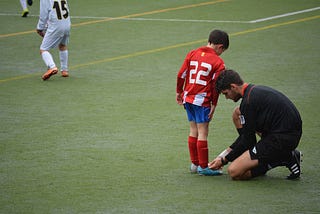 Football referee tying the laces of a young boy’s boots