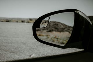 Looking back in a side mirror of a car, reflection of a hill, bushes, blurry, clear, no regrets.