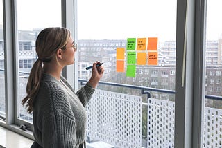 Woman holding a pen in front of some post it notes on a window.