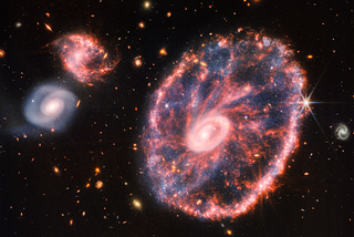 This new James Webb Telescope near and mid-infrared composite image highlights the Cartwheel Galaxy, the result of a high-speed collision that occurred about 440 million years ago, along with two neighboring galaxies.
