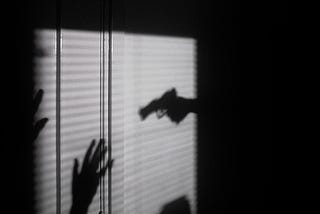 A silhouette holds another silhouette at gunpoint.