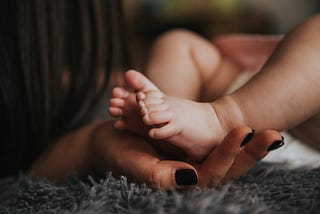 A mother’s hand holding the foots of her only child.