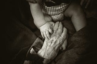 An elderly woman’s hand holding an infant’s.