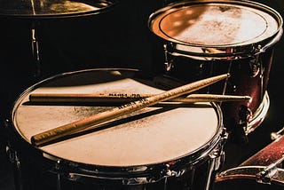 A well-worn drum set with a pair of drumsticks resting on it.