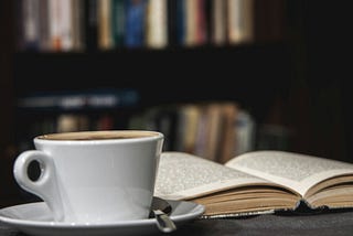 Coffee cup sitting next to an open book on a table