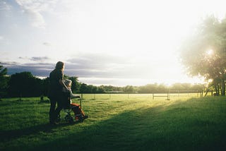 A younger woman pushes an old woman in a wheelchair on a field.