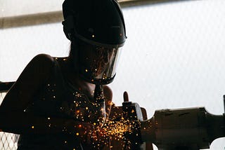A worker welds parts together while manufacturing machine parts.