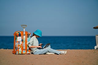 Girl remote worker sits on the beach with a suitcase and works while on vacation. IT specialist working online in time of eurotrip