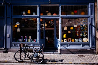 A blue storefront with lamps visible in the windows and a bike parked in front of the store.