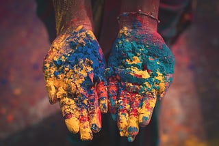 Colours of diverse citizens in a nation we weave in. Two hands coloured in Holi colours.