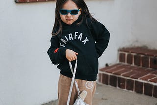 A female child charmingly posing for a picture while wearing sunglasses and holding a bag.