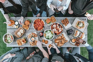 A family gathers around a wooden picnic table filled with delicious food.