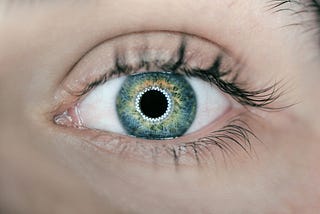 A close up image of a woman’s green eyes that seem to show matrix codes inside.